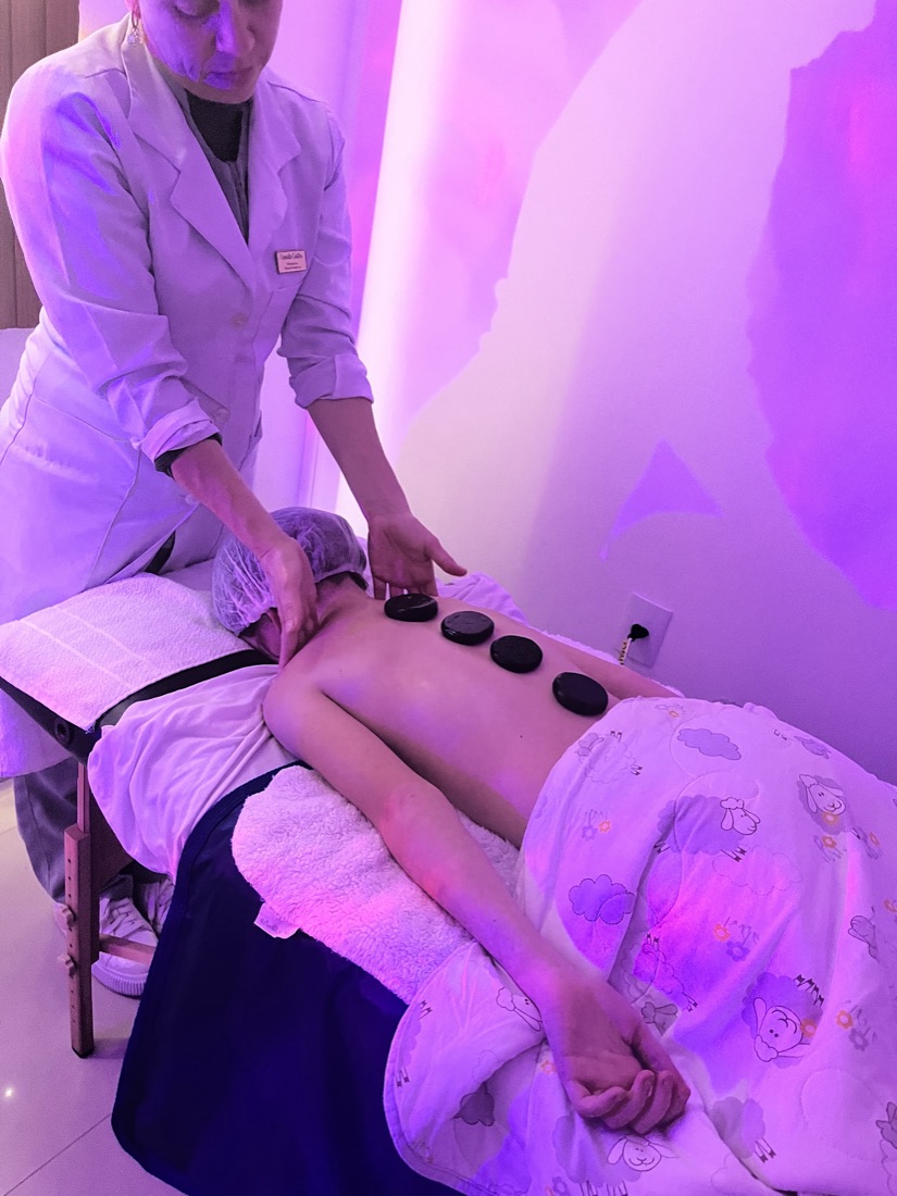 Massagem com pedras quentes nas costas, em sala com iluminação suave